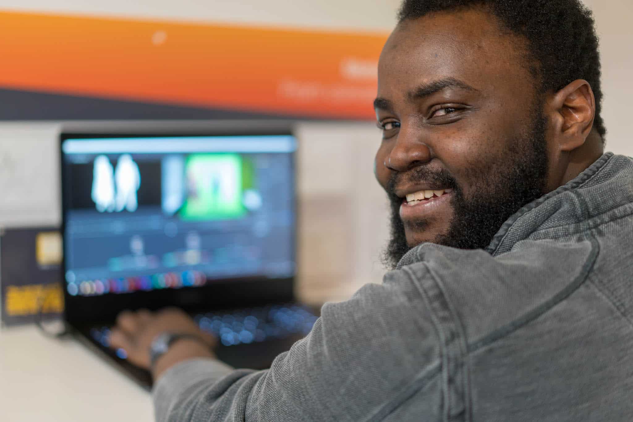 man smiling at camera whilst working on laptop