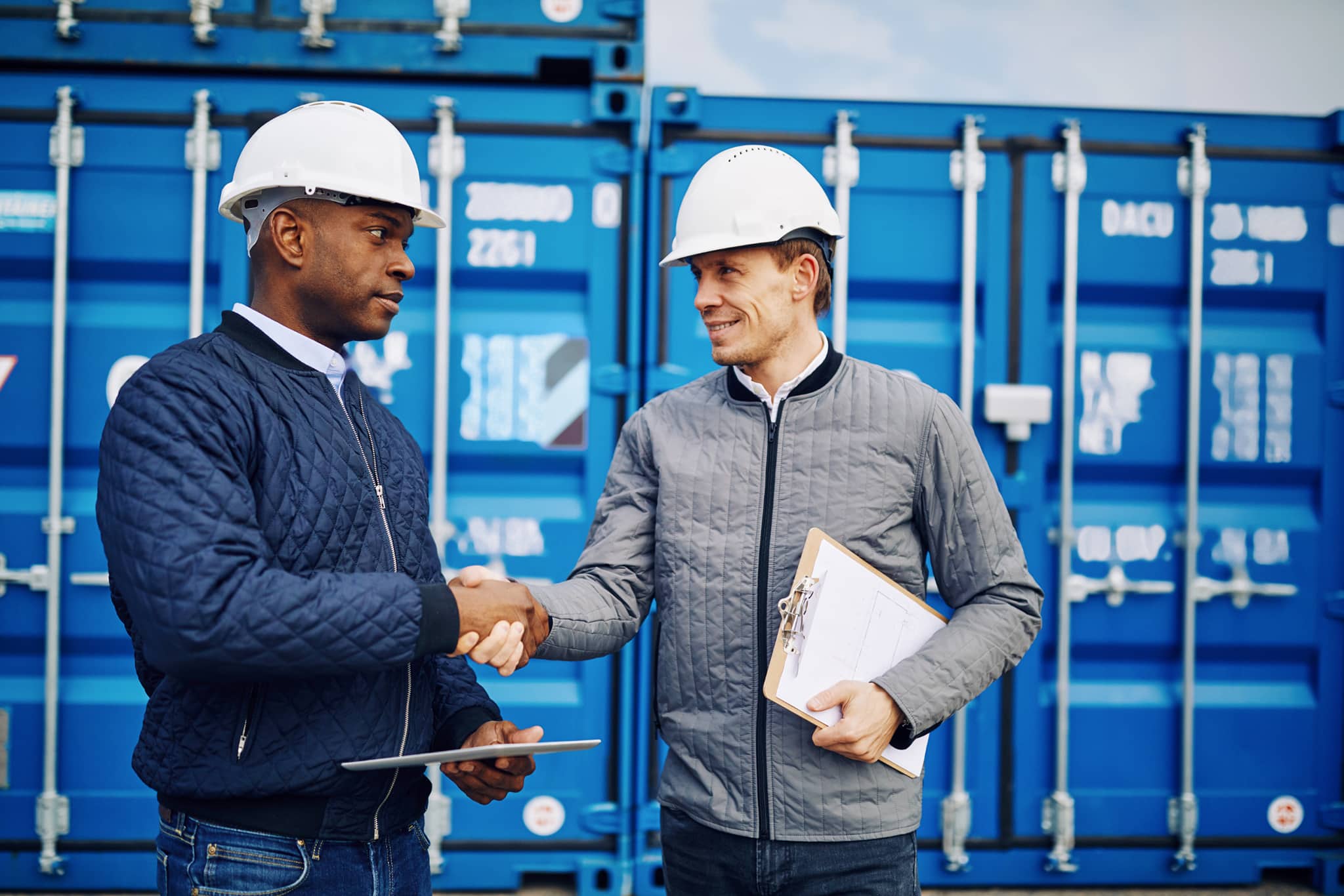 two men in building yard with hard hats, shaking hands